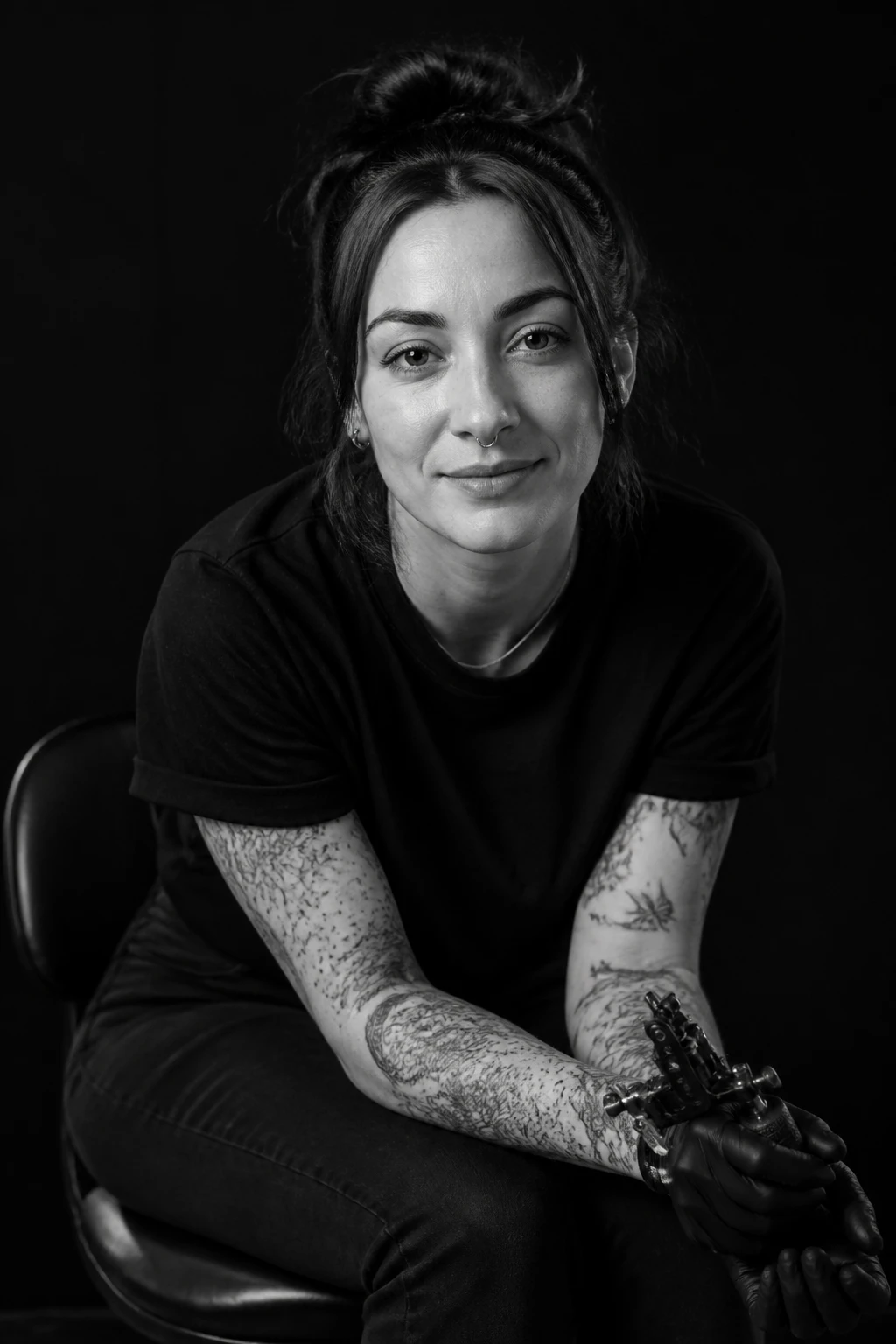 Retrato em preto e branco da tatuadora Marê Solá com tatuagens fine-line e dotwork nos antebraços, sorriso discreto
