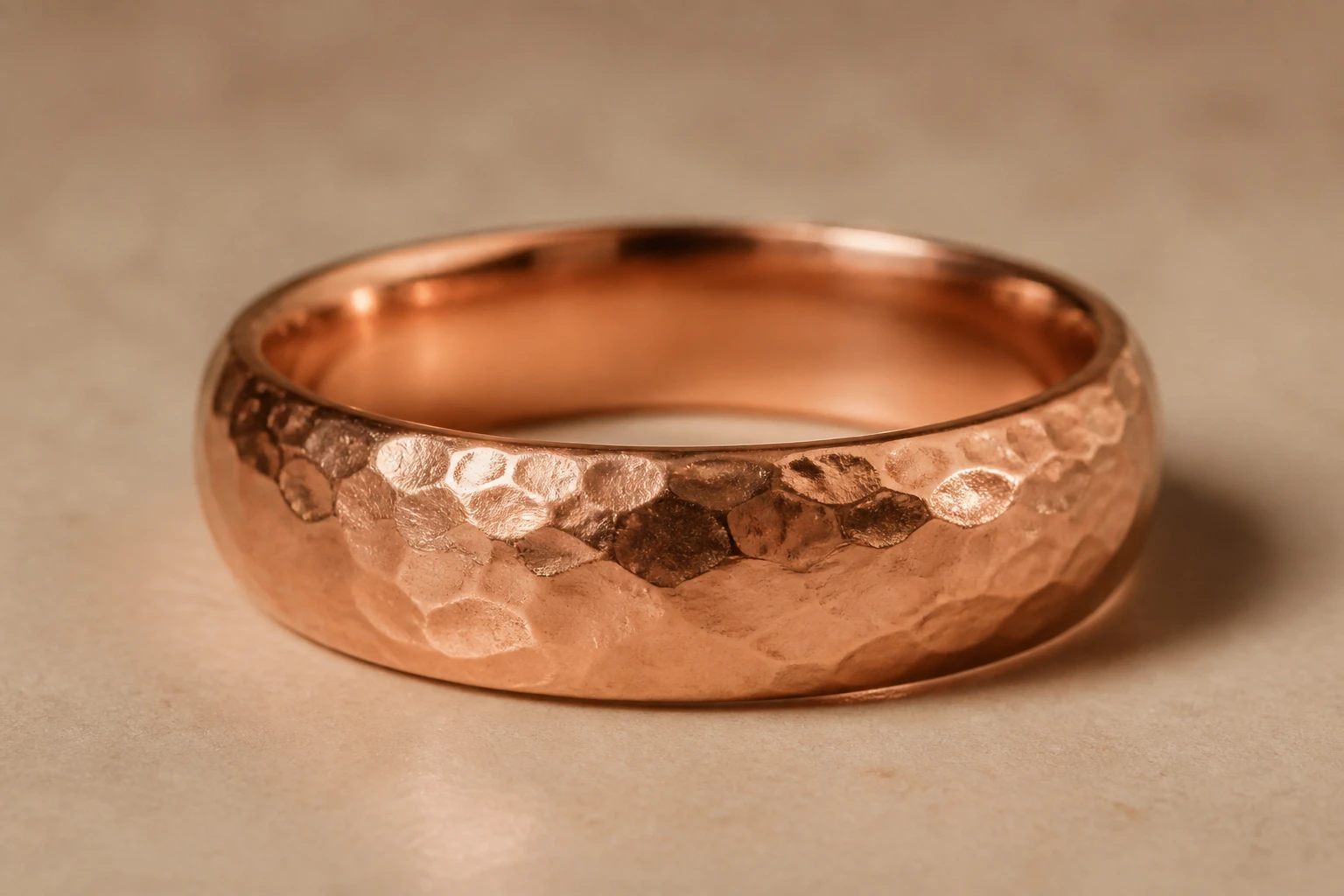 Aliança de ouro rosé texturizada à mão, com superfície orgânica irregular, em macro sobre fundo neutro