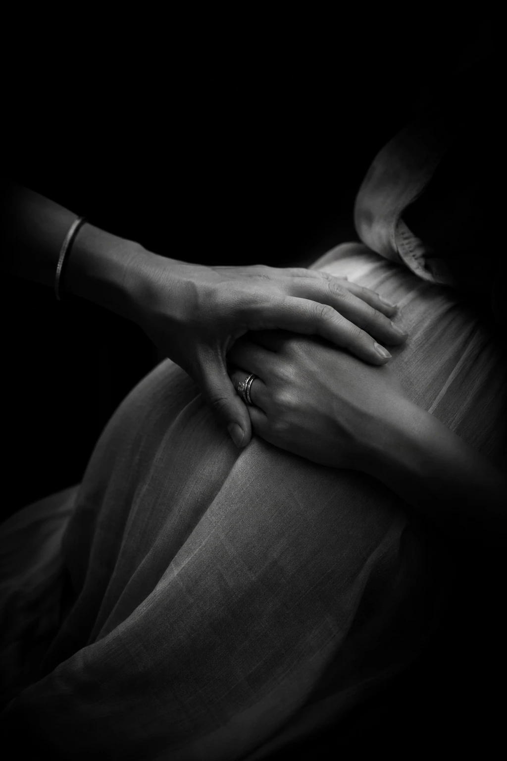 Retrato editorial em preto e branco de mãos serenas sobre tecido, luz baixa e dramática, presença e calma.