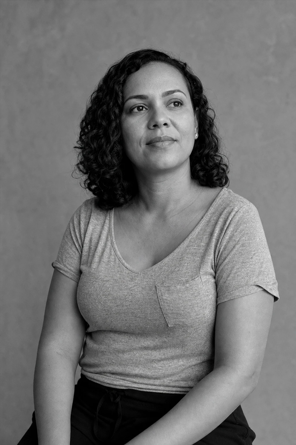Retrato editorial em preto e branco de uma mulher sentada, olhar sereno e firme voltado para a luz da janela
